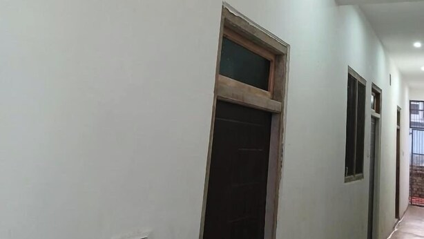 A corridor with white walls and a ceiling with recessed lighting. There are doors and windows along the walls. - Awadh Biharee Inn (Faizabad)