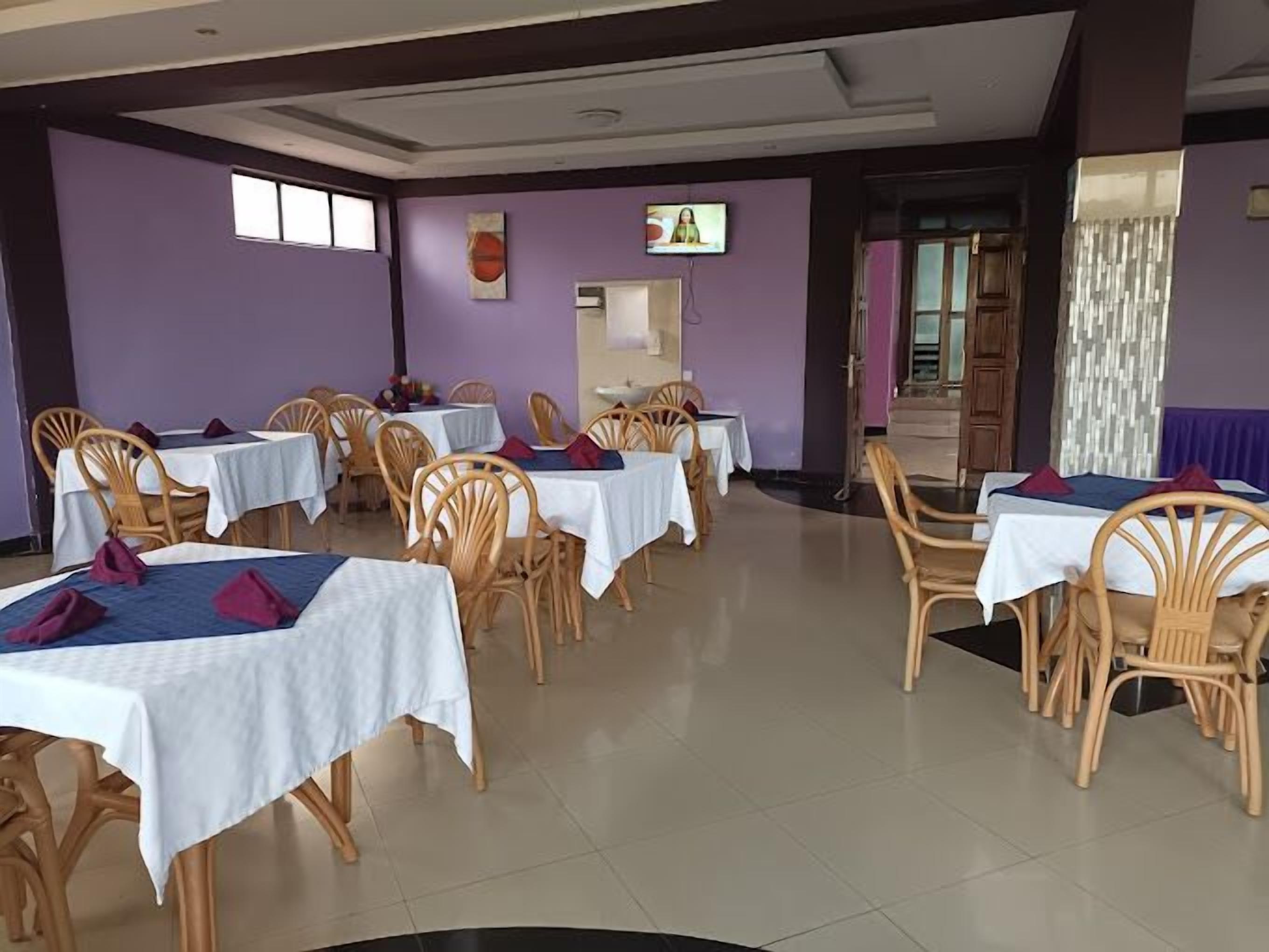 A dining area with multiple tables and chairs, a television mounted on the wall, and a door leading to another room.
