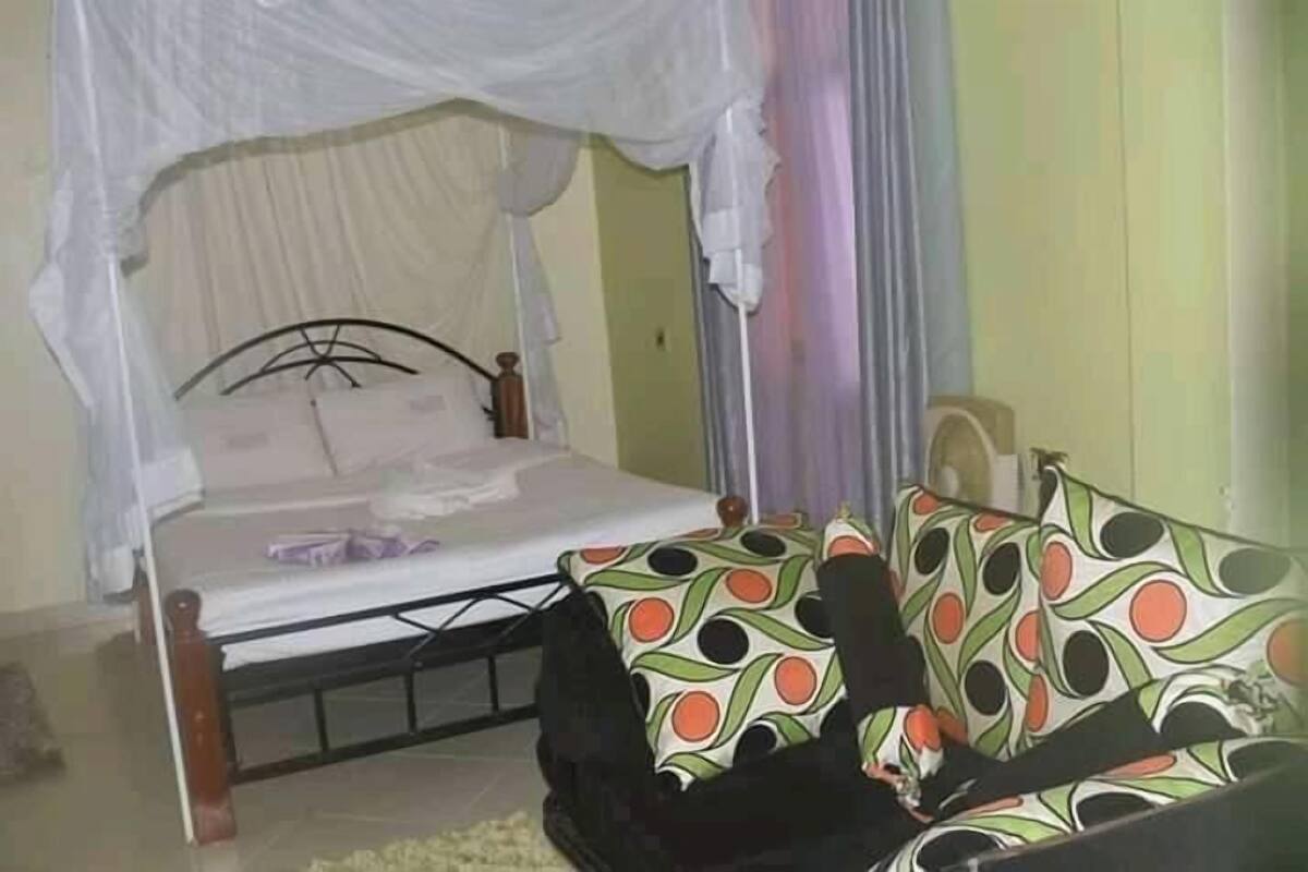 Quarto com cama sob dossel, sofá com almofadas estampadas e uma pequena mesa.