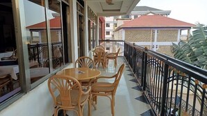 Un balcón con sillas y una mesa de madera, puertas de vidrio y vistas a edificios cercanos.