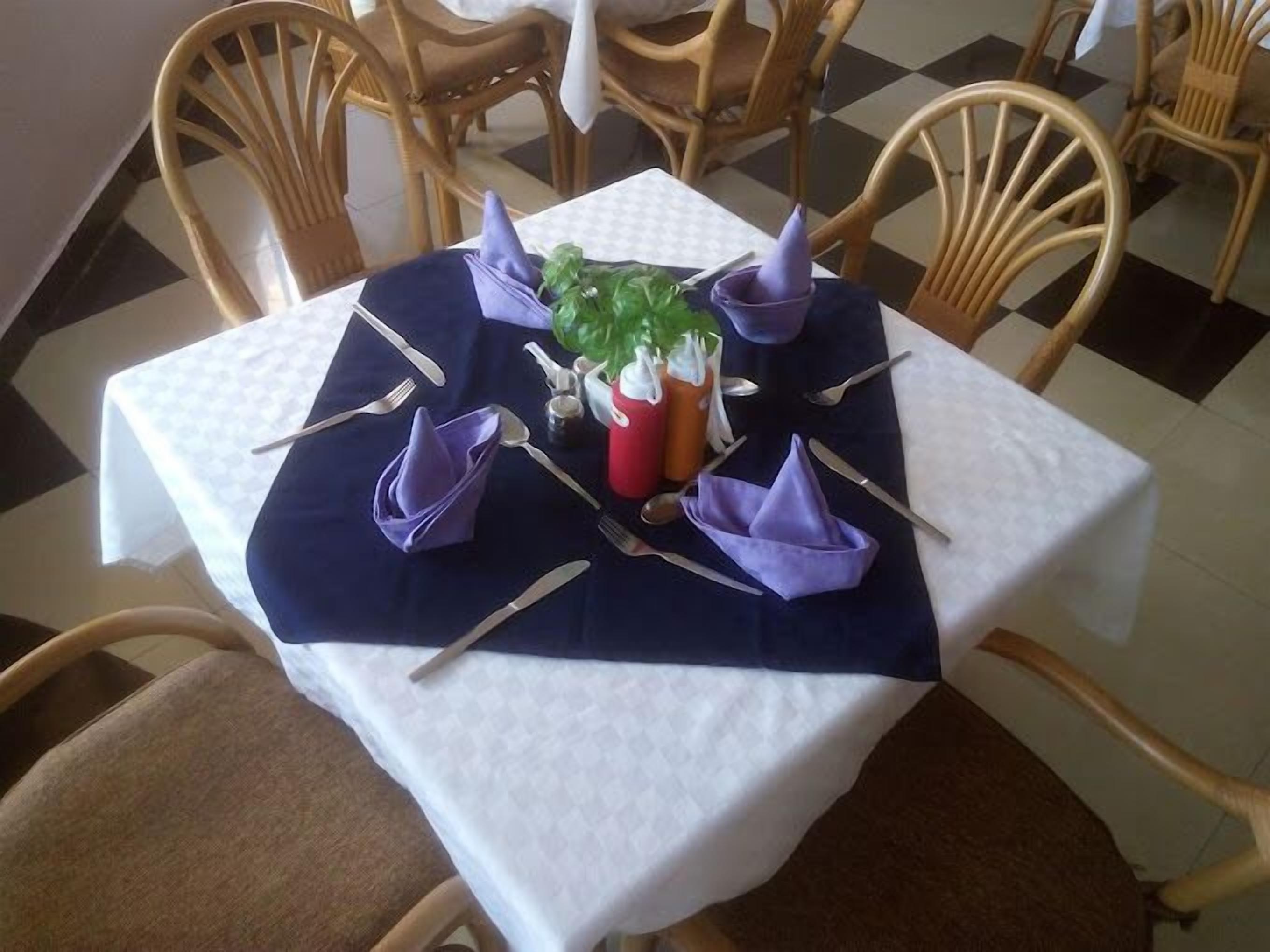 A dining table with a white tablecloth, dark blue placemat, and purple napkins.