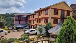 Un edificio de varios pisos con fachada amarilla y detalles en rojo, que cuenta con balcones y un estacionamiento con vehículos.