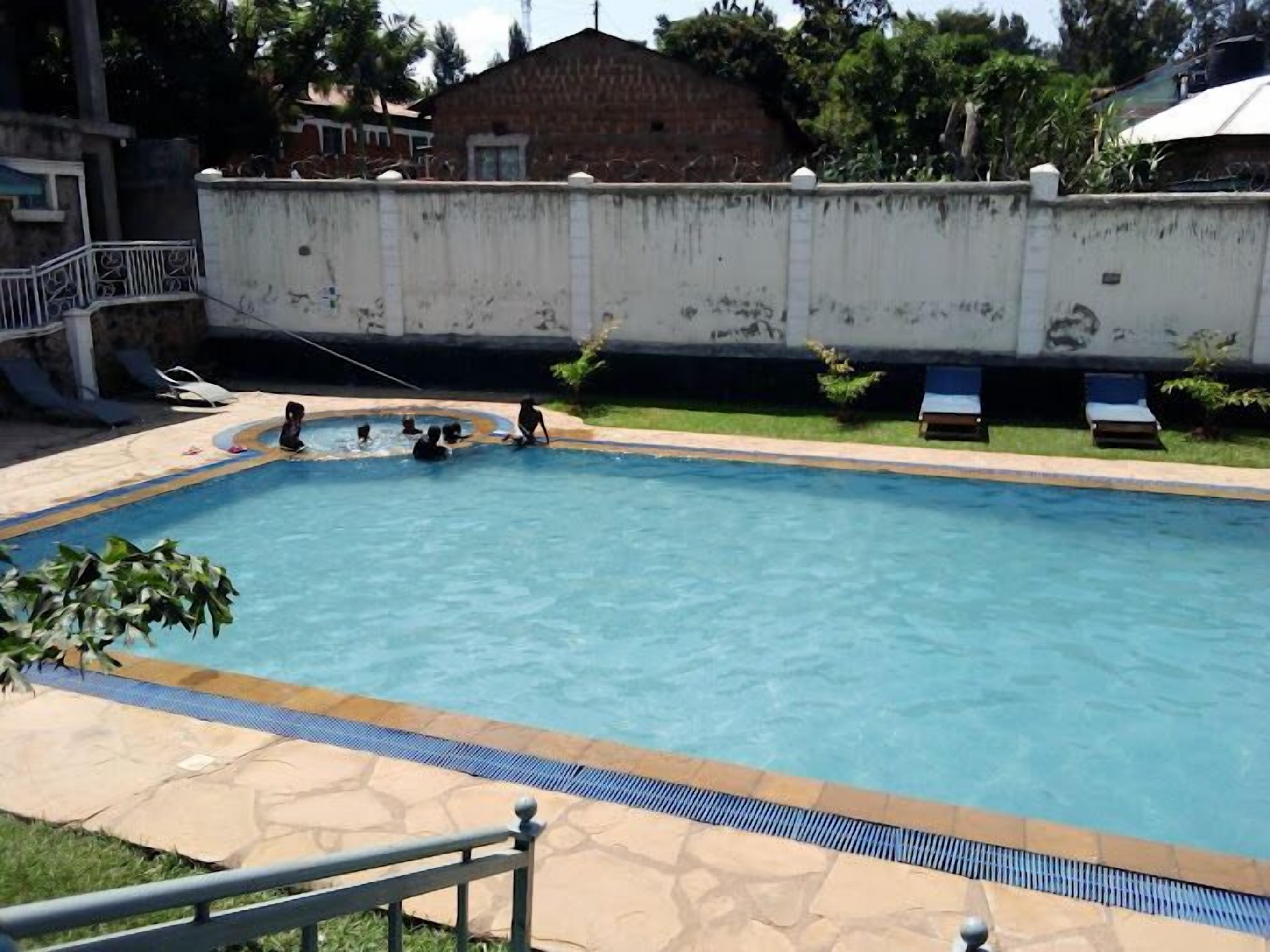 A rectangular swimming pool with a tiled deck, surrounded by a low wall and a few lounge chairs.