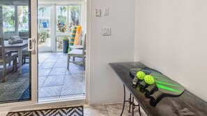A room with a sliding glass door leading to an outdoor area with a table and chairs, a small table with a bag, and a wall-mounted electrical outlet. - Luxury 3BR Key Largo Townhome | Ocean & Pool Views (Key Largo)