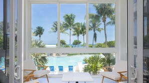 A room with a large window overlooking a pool and palm trees. - Luxury 3BR Key Largo Townhome | Ocean & Pool Views (Key Largo)