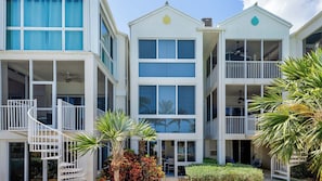 A multi-story building with balconies, large windows, and a small garden area with palm trees. - Luxury 3BR Key Largo Townhome | Ocean & Pool Views (Key Largo)