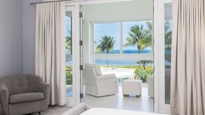 A modern bedroom with a large sliding glass door leading to a balcony with a view of the ocean and palm trees. - Luxury 3BR Key Largo Townhome | Ocean & Pool Views (Key Largo)