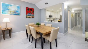 A dining area with a wooden table and chairs, a small side table with a lamp, and two paintings on the wall. - Luxury 3BR Key Largo Townhome | Ocean & Pool Views (Key Largo)