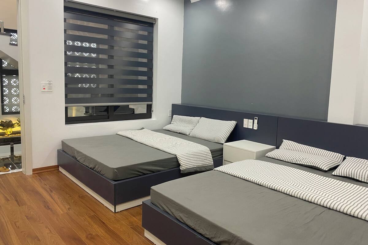 A modern bedroom with two single beds, a large window with blinds, and a built-in wardrobe.