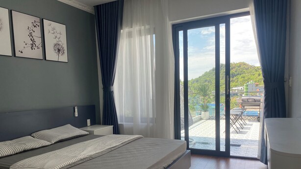 Une chambre moderne avec un grand lit, une vue sur un balcon agrémenté de mobilier d’extérieur et des œuvres d’art accrochées au mur.