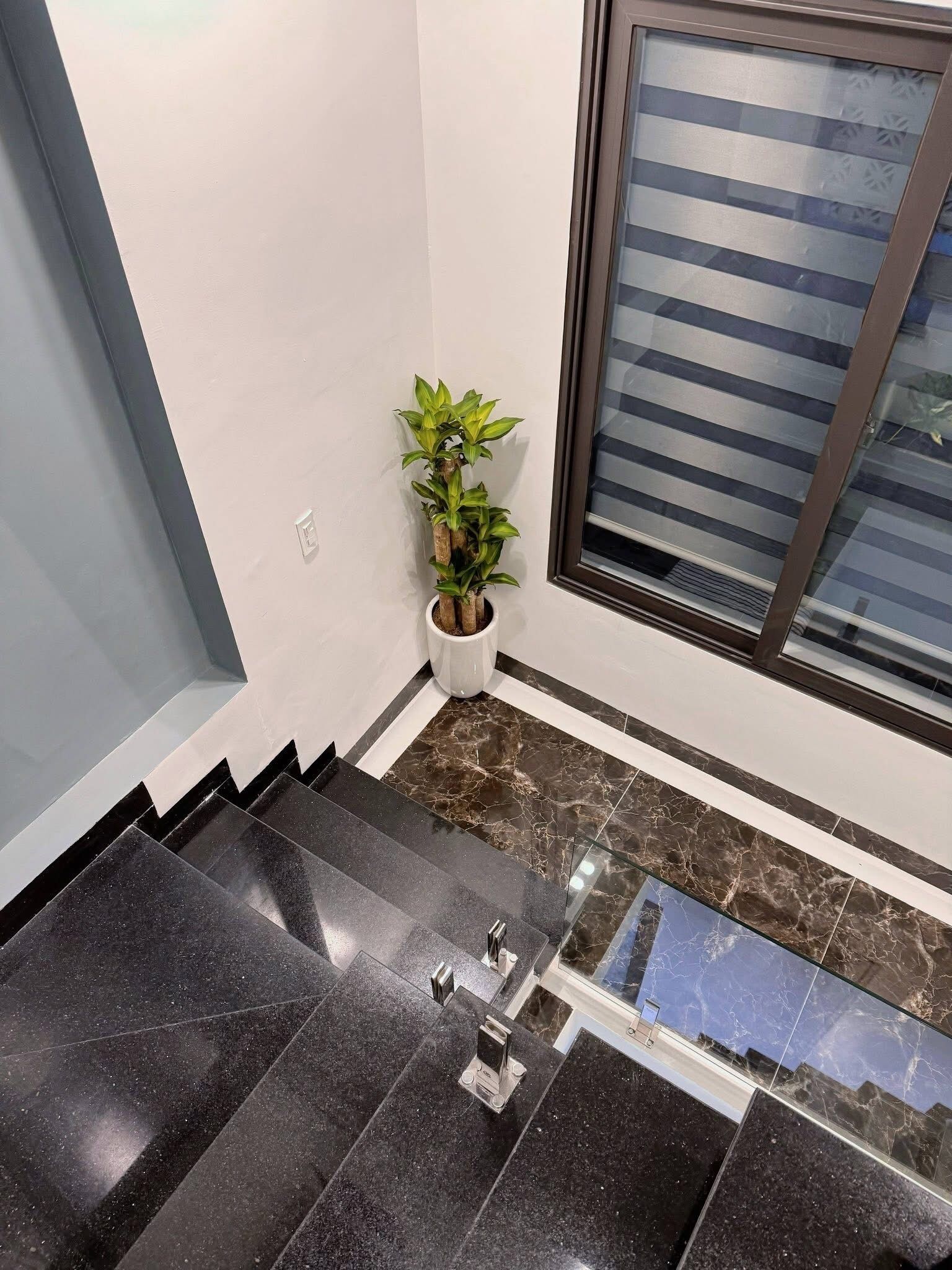 A modern staircase with black marble steps and a glass railing.