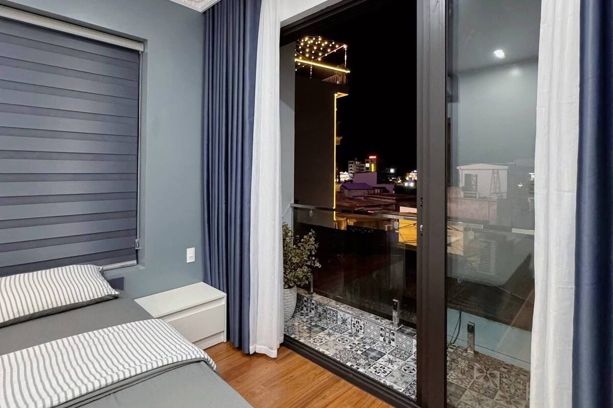 A modern bedroom with a large bed, a sliding glass door leading to a balcony, and a view of the city at night.