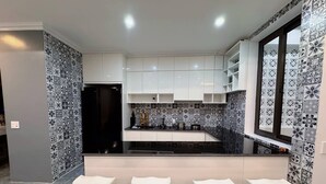 Une cuisine moderne avec des armoires blanches, un plan de travail noir et des carreaux décoratifs sur le mur derrière le plan de travail. On y trouve trois tabourets de bar blancs devant le plan de travail.