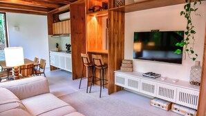 Un salon moderne avec un canapé, des éléments décoratifs en bois, un téléviseur et un coin repas comprenant des chaises et une table.