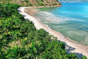A beach with clear turquoise waters, sandy shore, and lush green vegetation. - Casa Praia do Guaecá (Sao Sebastiao)