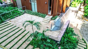 Un bâtiment moderne doté d’une façade en bois, d’un escalier menant à l’entrée et d’un jardin bien entretenu où poussent différentes espèces de plantes.