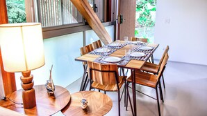 Un coin repas avec une table en bois dressée pour quatre personnes, entourée de chaises en bois, d’une maquette de bateau et d’une lampe.
