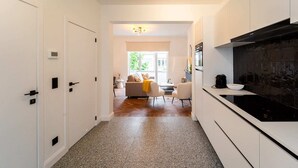 Une cuisine moderne avec des meubles blancs, une plaque de cuisson noire et un coin repas comprenant un canapé et des chaises.