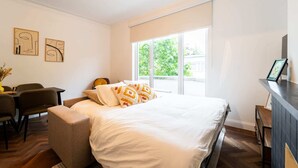 Une chambre d’hôtel moderne, dotée d’un grand lit, d’un bureau et d’une chaise. Une fenêtre offre une vue sur la verdure environnante.