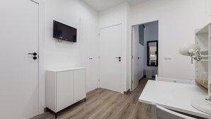 Ein heller, moderner Flur mit weißen Wänden und Holzboden, der zu einem Küchenbereich mit weißer Arbeitsplatte und Spüle führt.