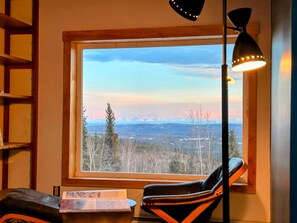 Enjoy a panoramic view of the mountains from the comfort of this room, featuring a cozy chair and floor lamp.
