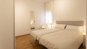 Ein Hotelzimmer mit zwei Betten, Holzboden, einem großen Spiegel und einem Sessel.
