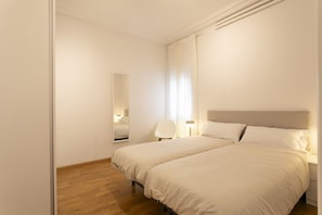 Hotellihuone, jossa on kaksi sänkyä, puulattia, suuri peili ja tuoli.