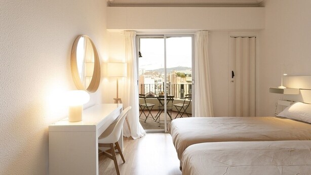 Ein Hotelzimmer mit zwei Betten, einem Schreibtisch, einem Stuhl, einem Spiegel und einem Balkon mit Tisch und Stühlen.