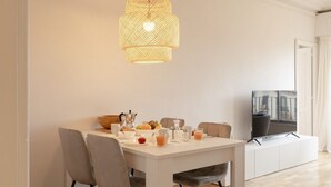 Ein zeitgemäßer Essbereich mit einem weißen Tisch, grauen Stühlen und einer gewebten Pendelleuchte.