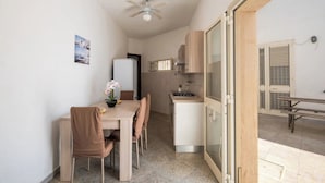 Eine kompakte Küche mit Mikrowelle, Herd und Schränken. Ein Esstisch mit Stühlen und ein Deckenventilator sind vorhanden. Eine Glasschiebetür führt zu einem Außenbereich mit einer Sitzbank.