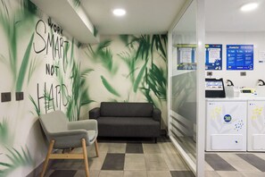 Un área de espera con sofá y sillones, una pared con una cita motivacional y un quiosco de autoservicio.