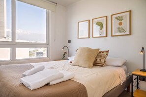 Een slaapkamer met een groot bed, nachtkastje, lamp en kunstwerken in een lijst op de muur.