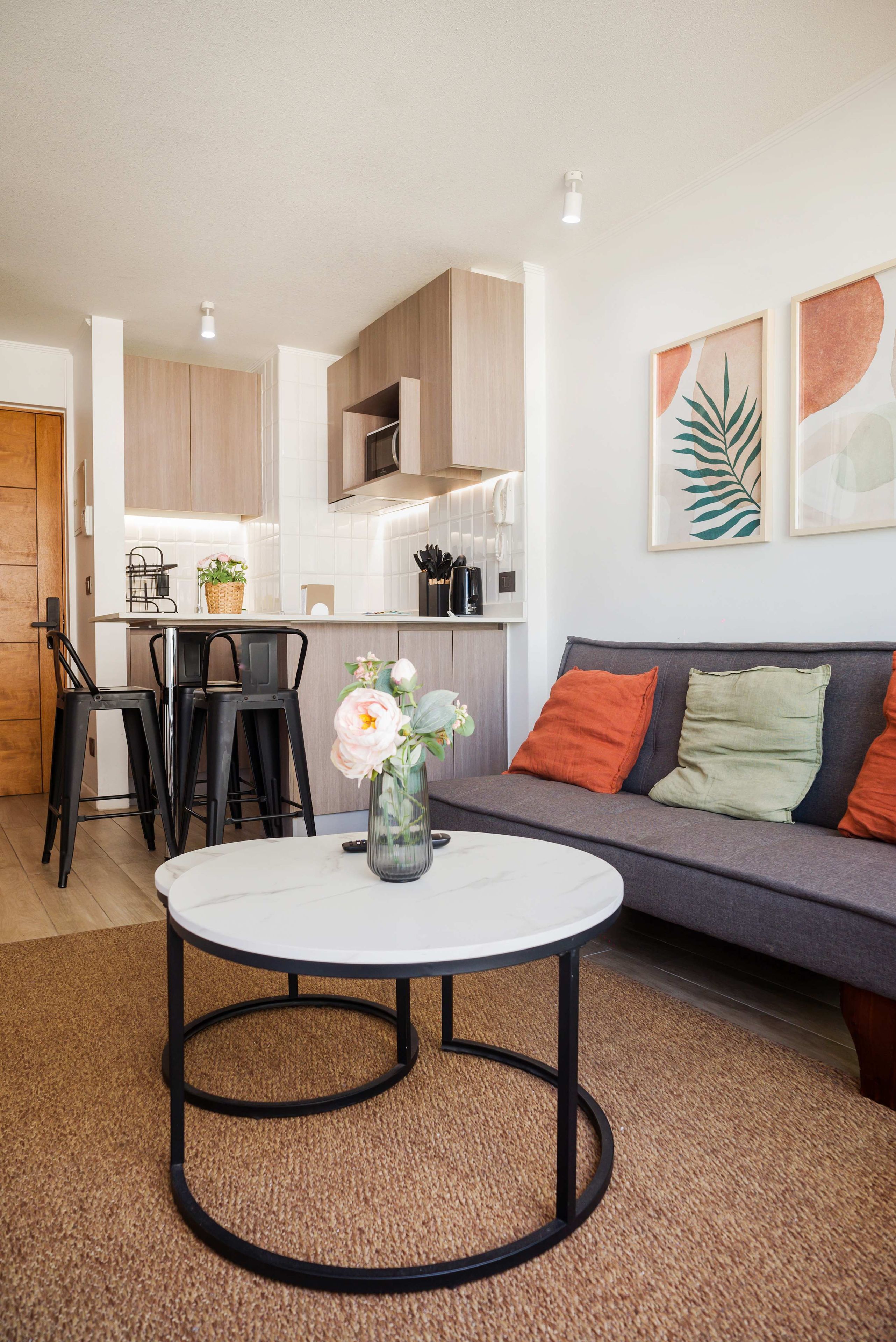 A modern living room with a round table, a sofa with cushions, a kitchen area, and a dining space.