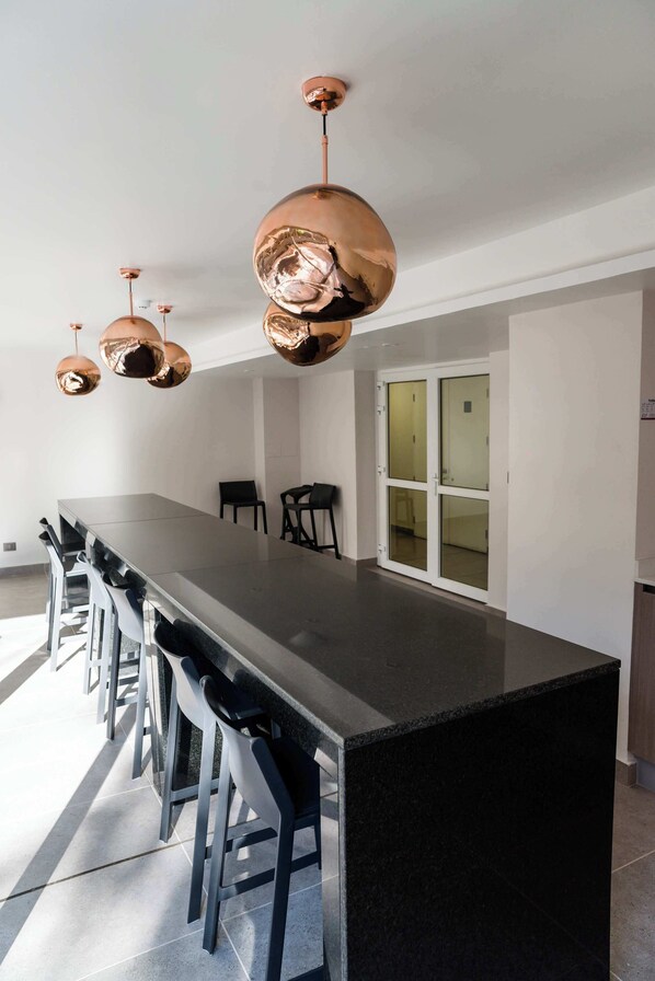 Une cuisine moderne dotée d’un grand îlot central, de tabourets de bar noirs et de luminaires suspendus en cuivre.