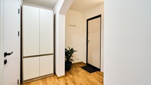Un pasillo con piso de madera, un armario blanco, una planta en maceta y una puerta con felpudo negro.