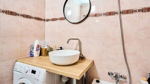 Un baño con lavadora, un lavabo con espejo y ducha.