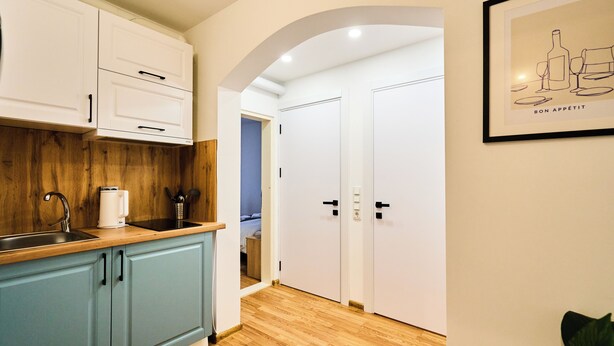 Una cocina moderna con armarios azul claro, encimera de madera y una cafetera. Hay un cuadro en la pared y una puerta que da a otra habitación.