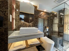 Un baño moderno con tocador de mármol, un espejo grande, cabina de ducha de vidrio y un inodoro blanco.