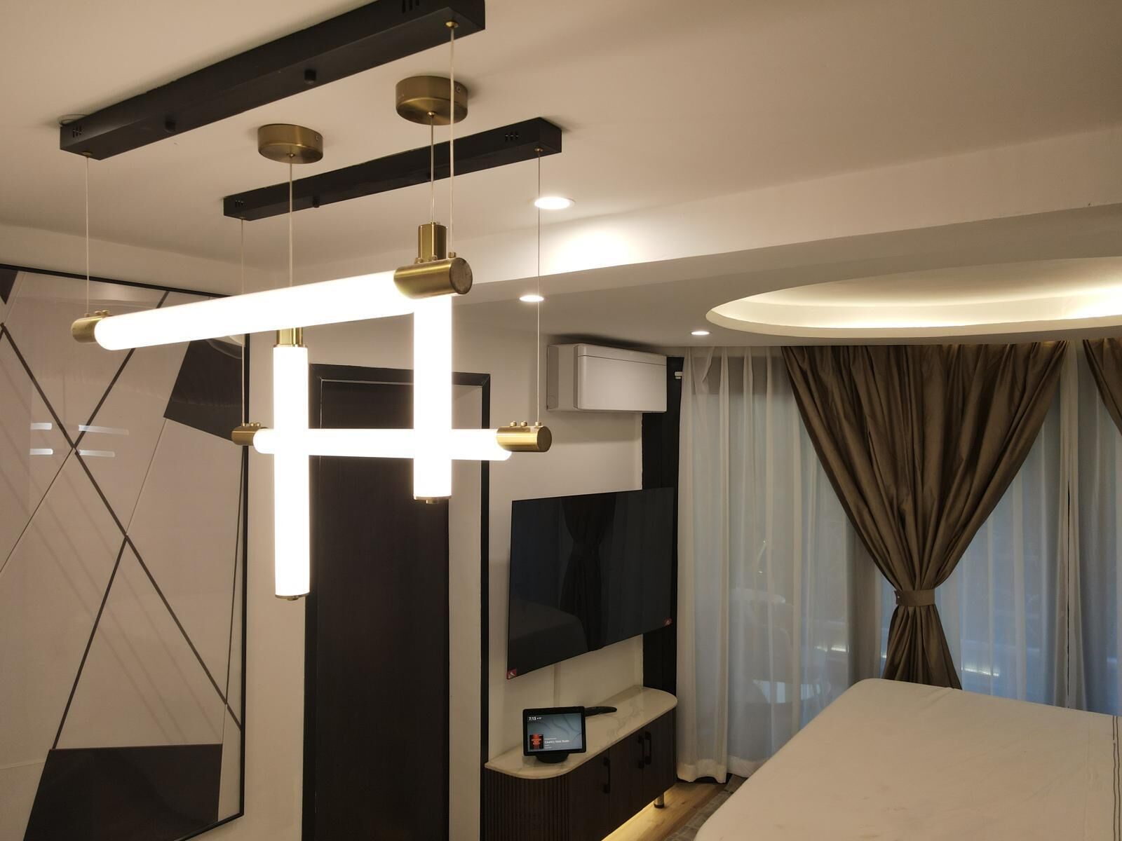 A modern hotel room with a bed, a desk with a computer, a TV, and a large mirror.