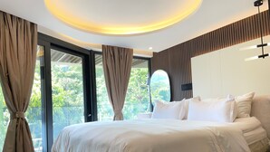 A modern bedroom with a large bed, a ceiling light, and a view of greenery outside. - Vita Resort Golf Bastos (Yaoundé)