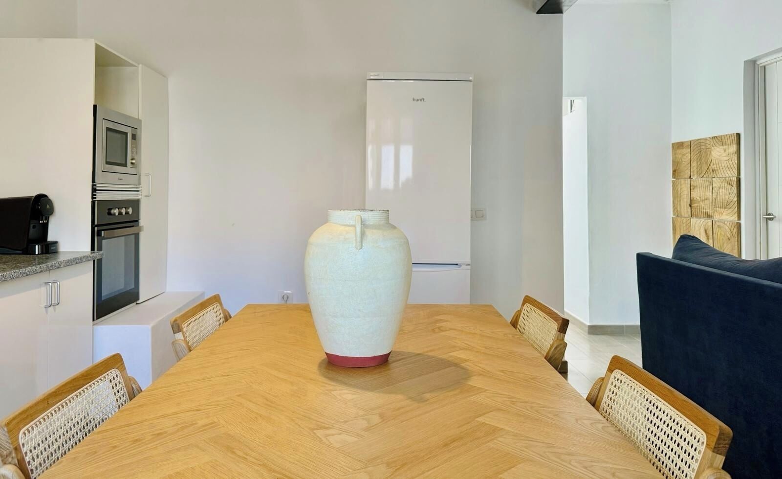 Una cocina moderna con electrodomésticos integrados, una mesa de comedor con sillas y un gran jarrón como centro de mesa.