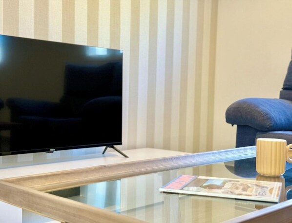 Una sala de estar moderna con un televisor de pantalla plana sobre una mesa de centro de vidrio, un fondo de papel tapiz a rayas y un sofá azul.