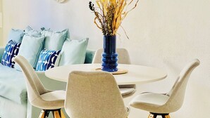Un comedor con una mesa redonda, cuatro sillas grises y un jarrón azul con plantas secas.