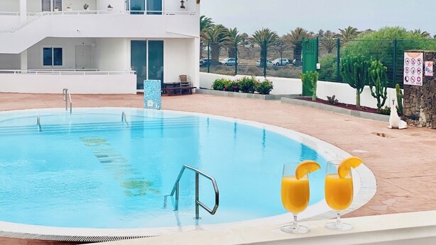 Una piscina con escalera metálica, un edificio blanco con balcones y un cartel con símbolos.