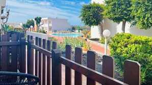 Zona de piscina con valla de madera, plantas en macetas y un cielo azul despejado.