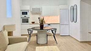 A modern kitchen with white cabinets, a dining table with chairs, and a refrigerator. - Canaryislandshost I Cactus II (Mala)