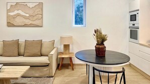 A modern living room with a sofa, a round table, a lamp, and a vase with dried flowers. There is a window with a view of trees and an air conditioning unit on the wall. - Canaryislandshost I Cactus II (Mala)