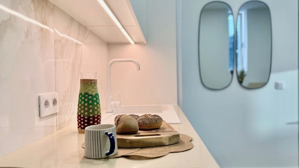 A modern bathroom with a marble wall, a towel rack, a glass bottle, a mug, and a wooden tray with bread. - Canaryislandshost I Cactus II (Mala)