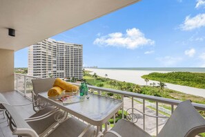 A balcony with a table, chairs, and a view of the beach and ocean. - Sw-facing Beachfront Condo With Pool/gym/pickleball (Marco Island)