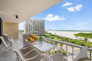 A balcony with a table, chairs, and a view of the ocean and a hotel in the background. - Sw-facing Beachfront Condo With Pool/gym/pickleball (Marco Island)